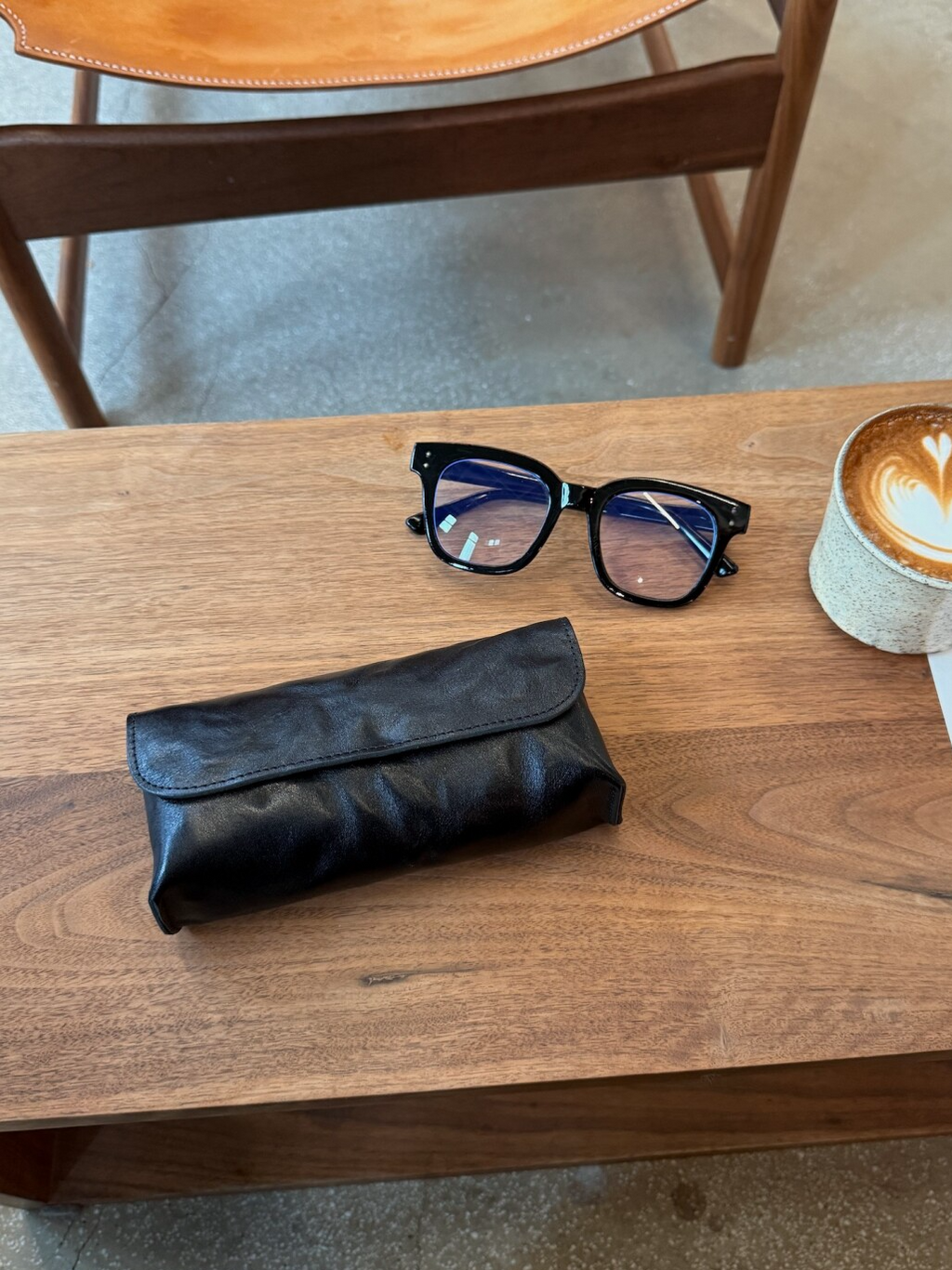 Black eyeglass case and glasses on a wooden table with a coffee cup in the background