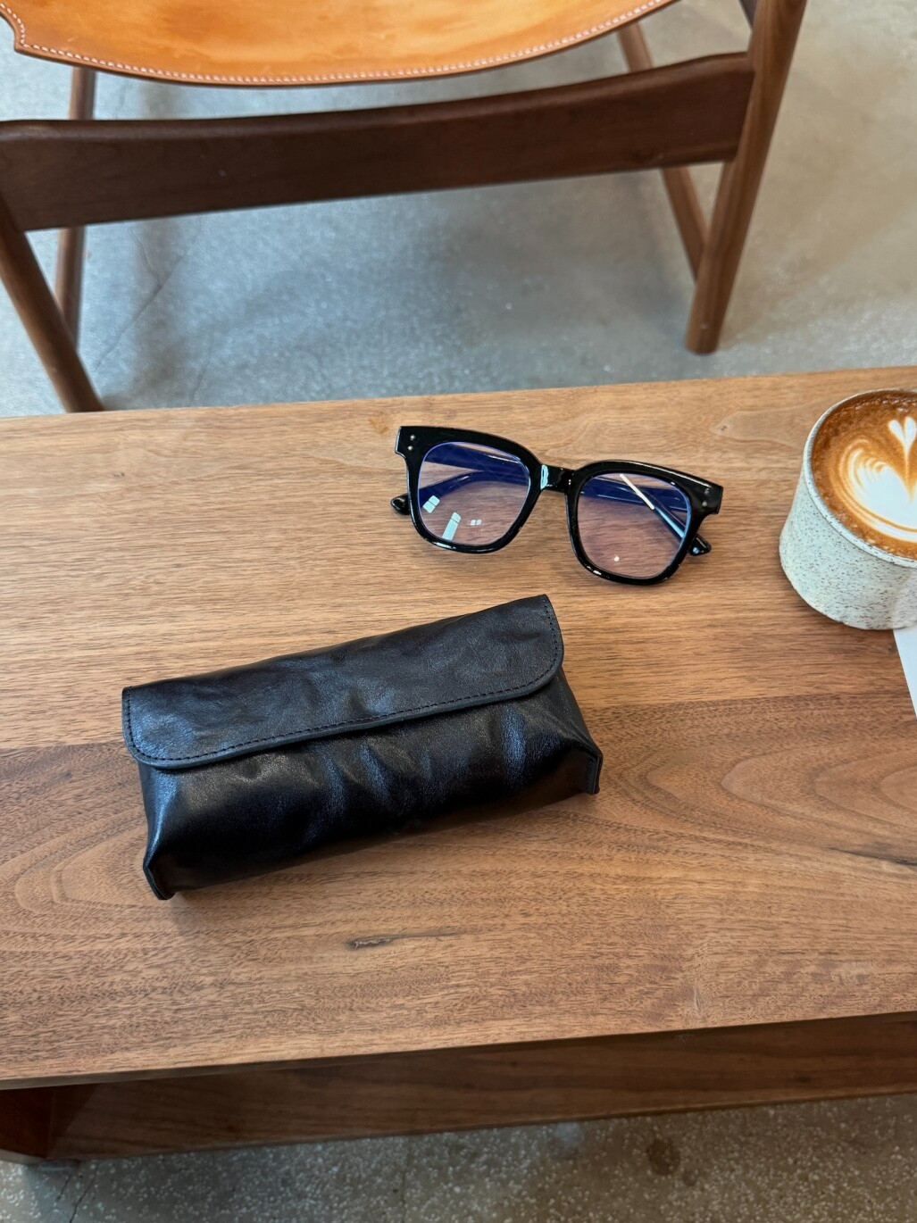 Black eyeglass case and glasses on a wooden table with a coffee cup in the background