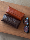 Two leather cases, sunglasses, a cup of coffee with a latte art design, and a receipt on a wooden table.
